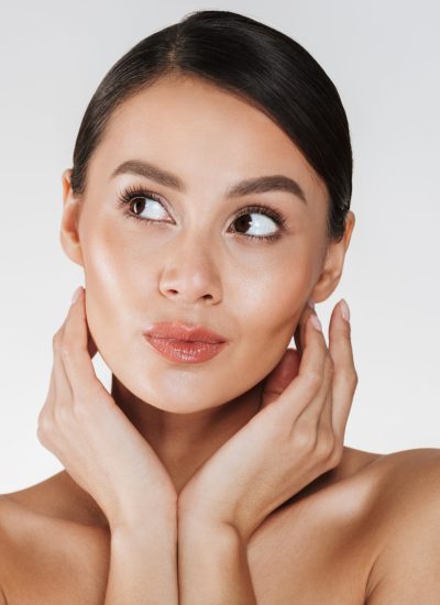 Close up portrait of beautiful woman with natural makeup looking aside and holding hands close to her healthy face isolated over white background
